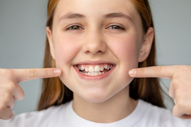 Dziewczyna uśmiecha się i pokazuje jej nierówne zęby dłońmi stomatologia i opieka zdrowotna