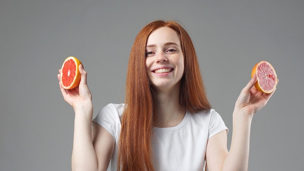 Dziewczyna uśmiecha się i trzyma połówki grejpfruta na szarym tle