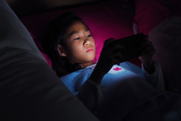 Dziewczyna używa telefon komórkowego na ciemnym łóżku w sypialni