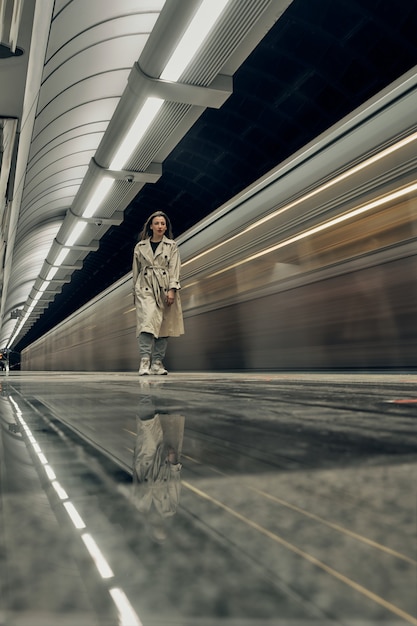 Zdjęcie dziewczyna w beżowym trenczu w metrze czeka na pociąg na peronie