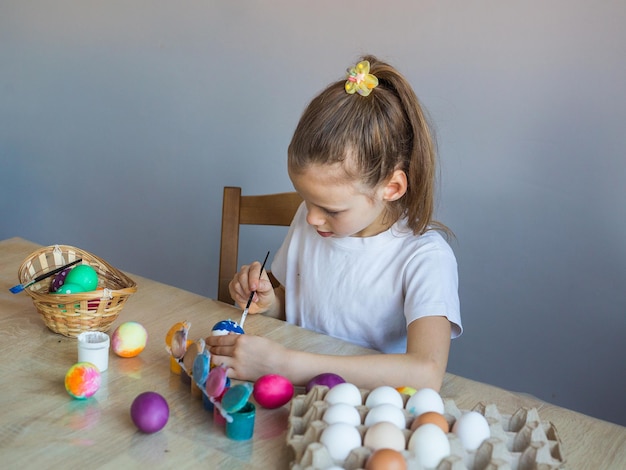 Dziewczyna w białej koszulce maluje pisanki farbami i pędzlem Wiosna Malowane jajka