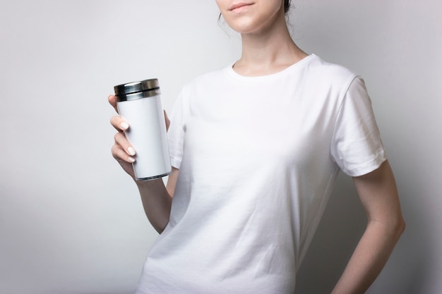 Dziewczyna w białej koszulce trzyma kubek z kawą. Puste dla marki. Makieta monochromatyczna