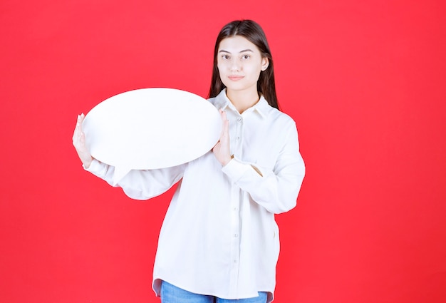 Dziewczyna w białej koszuli trzymająca owalną tablicę informacyjną