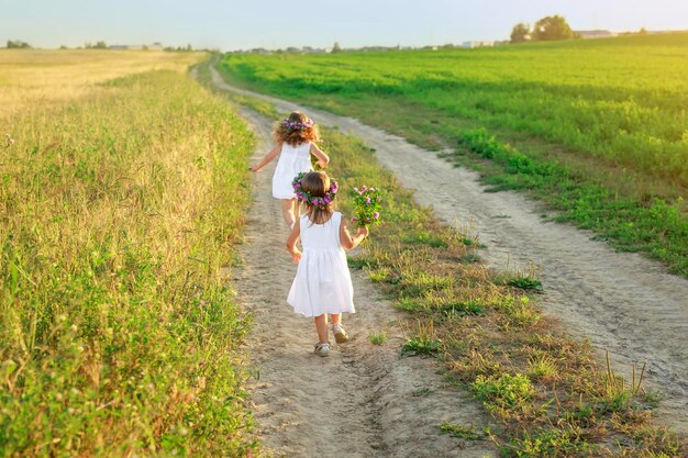 Dziewczyna w białej sukience dogania siostrę biegnącą piaszczystą drogą na pole