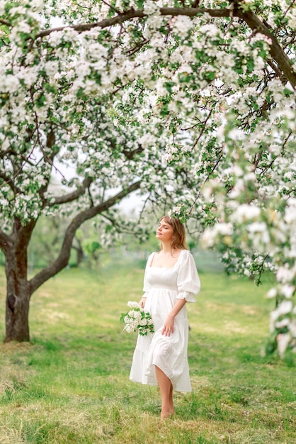 Zdjęcie dziewczyna w białej sukience w ogrodzie wiosennym z bukietem kwiatów.