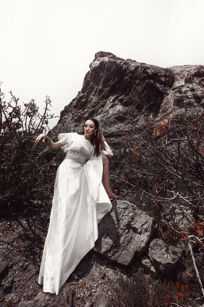 Dziewczyna w białej sukni stawia boso stopę na kamieniu, wśród skał