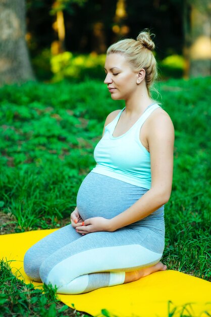 Dziewczyna w ciąży siedzi na macie do jogi w parku po treningu
