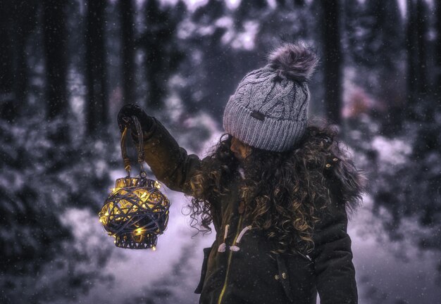 Zdjęcie dziewczyna w ciepłych ubraniach trzymająca oświetloną latarnię