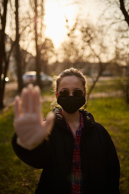 Zdjęcie dziewczyna w czarnej masce medycznej pokazuje ręką znak stop