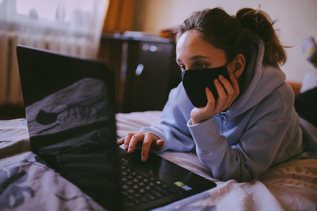 Dziewczyna w czarnej masce pracuje na laptopie w domu w izolacji, kwarantanna obróbka zdjęć vintage