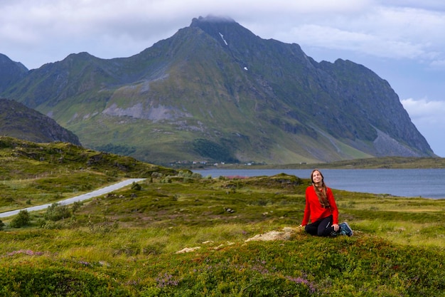 dziewczyna w czerwonej bluzie siedzi na mchu pod ogromnymi klifami norweskich fiordów, panorama lofotów