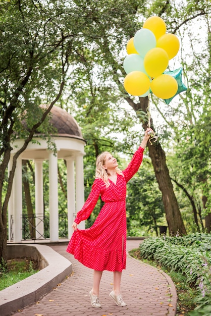 Dziewczyna w czerwonej sukience i kilka kolorowych balonów w parku