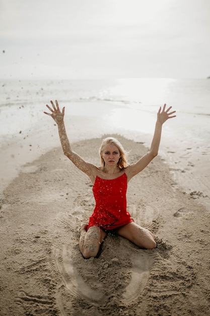 Zdjęcie dziewczyna w czerwonej sukience rzuca biały piasek morski
