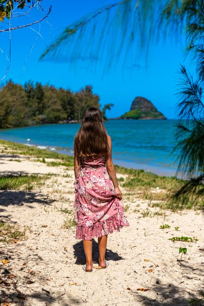 Zdjęcie dziewczyna w długiej sukience spaceruje wzdłuż wybrzeża w parku regionalnym kualoa na oahu na hawajach, z widokiem na mokolii