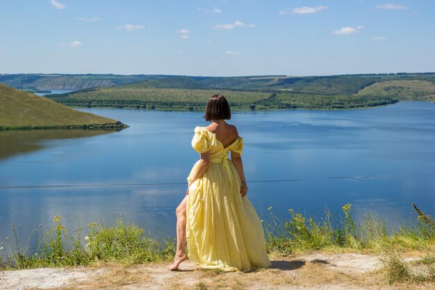 Dziewczyna w długiej sukni stojąca na klifie nad zatoką