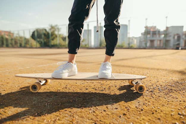 Dziewczyna w dżinsach i tenisówkach stoi na longboardzie na tle boiska do koszykówki