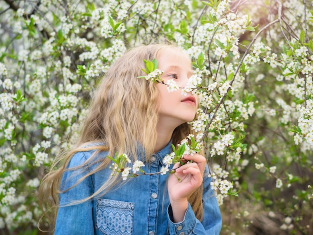 Dziewczyna w dżinsowej koszuli cieszy się zapachem wiśniowych kwiatów