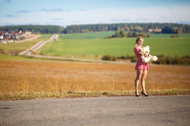 Dziewczyna w garniturze w kratę zostaje na asfaltowej drodze z misiem koncepcją samotności czekającej na szczęście