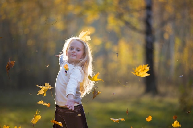 Dziewczyna w jesiennym parku rozrzuca liście klonu Dziecko na spacerze jesienią