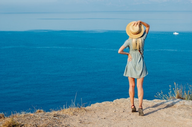 Dziewczyna w kapeluszu nad morzem na skraju urwiska.