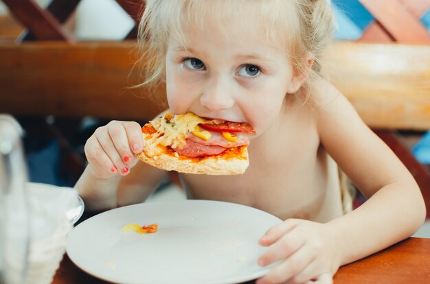 Dziewczyna w kawiarni je pizzę z kiełbasą