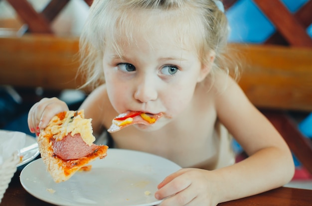 Dziewczyna w kawiarni je pizzę z kiełbasą