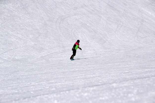 Dziewczyna w kolorowym garniturze na snowboardzie jeździ po górach