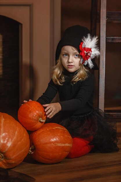 Zdjęcie dziewczyna w kostiumie czarownicy siedzi w pobliżu kominka i bawi się dyniami halloween vertical frame