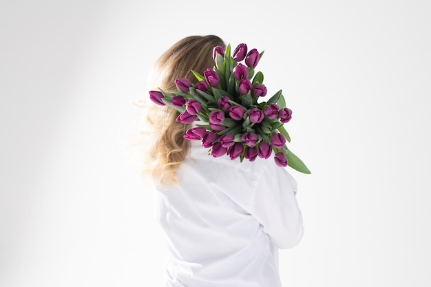 Dziewczyna w koszuli położyła na ramieniu mnóstwo białych i fioletowych tulipanów różnych odmian
