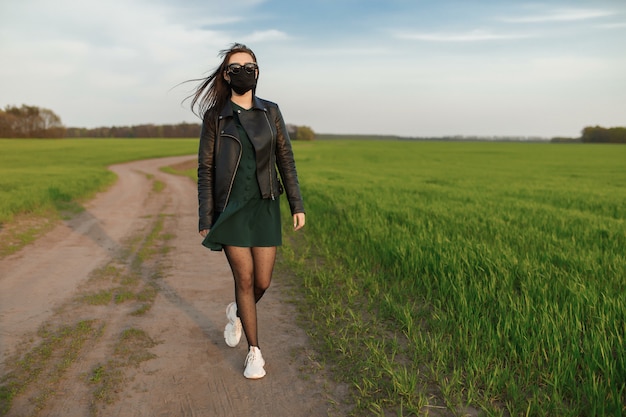 Dziewczyna w medycznej masce biegnie lub chodzi po zielonym polu. Poddaj kwarantannie wiosenne lato. koronawirus