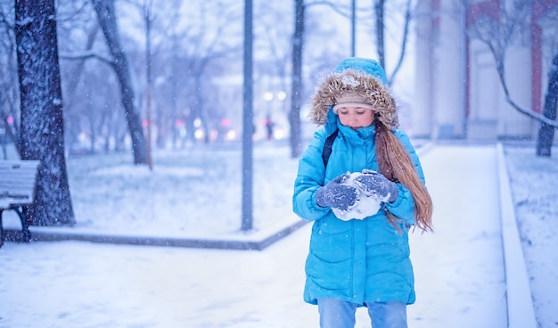 Zdjęcie dziewczyna w niebieskich zimowych ubraniach bawi się śniegiem w winter park.