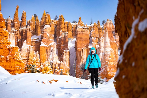 dziewczyna w niebieskiej kurtce wędrująca przez zaspy śnieżne wśród masywnych skał kanionu bryce w mroźną zimę