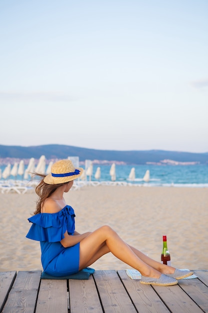 Dziewczyna w niebieskiej sukience siedzi na piaszczystej plaży