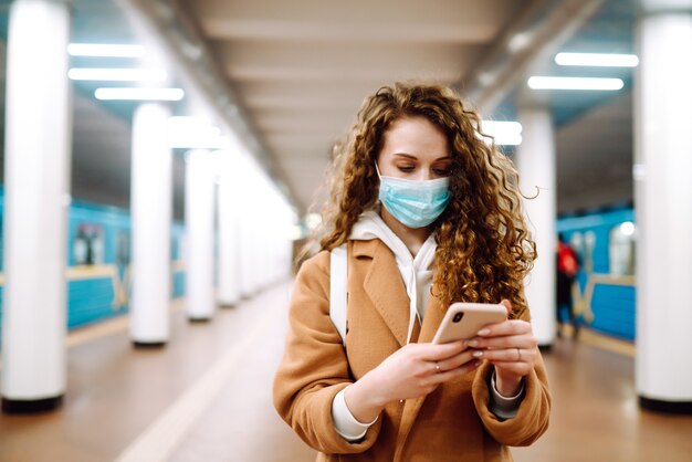 Dziewczyna w ochronnej sterylnej masce medycznej z telefonem na stacji metra