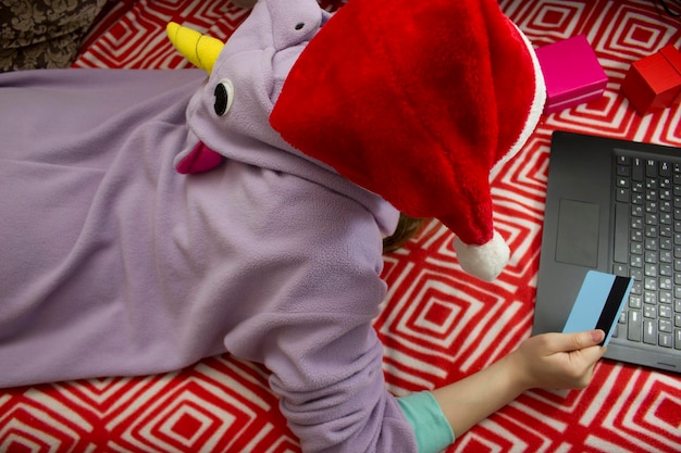 Zdjęcie dziewczyna w piżamie i santa hat zakupy online za pomocą karty kredytowej.