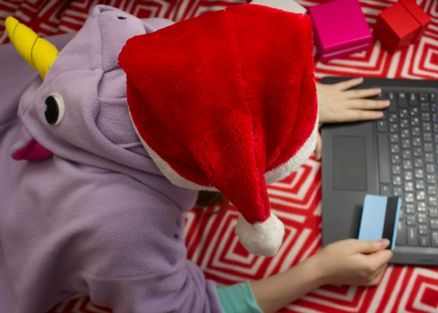 Dziewczyna w piżamie i santa hat zakupy online za pomocą karty kredytowej.