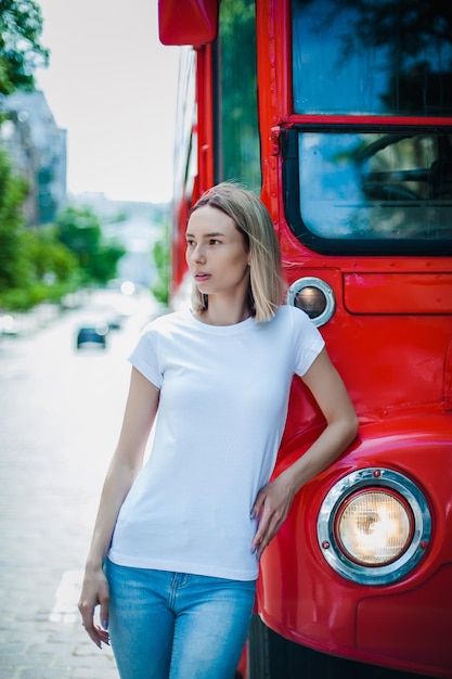Dziewczyna w pustej białej koszulce i dżinsach stoi w pobliżu makiety autobusu dla drukarni tshirt