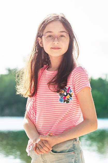 Zdjęcie dziewczyna w różowej koszulce w paski i dżinsowej spódnicy nad rzeką latem. nastolatek dziewczyna w przyrodzie.