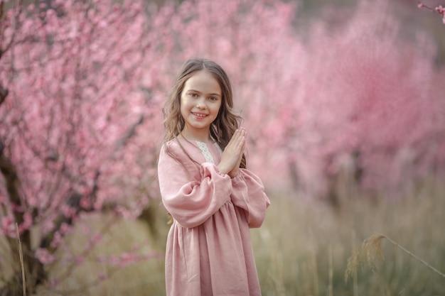 Dziewczyna w różowej sukience w kwitnącym ogrodzie z różowymi drzewami