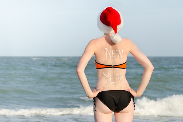 Dziewczyna w Santa kapeluszach z napisem Nowy Rok na plecach. Brzeg morza. Widok z tyłu