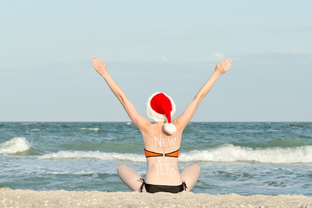Dziewczyna w Santa kapelusze na brzegu morza. Podniósł ręce.