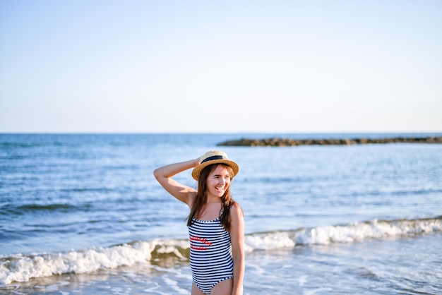 dziewczyna w słomkowym kapeluszu i pasiastym stroju kąpielowym, ciesząca się widokiem na morze z tyłu