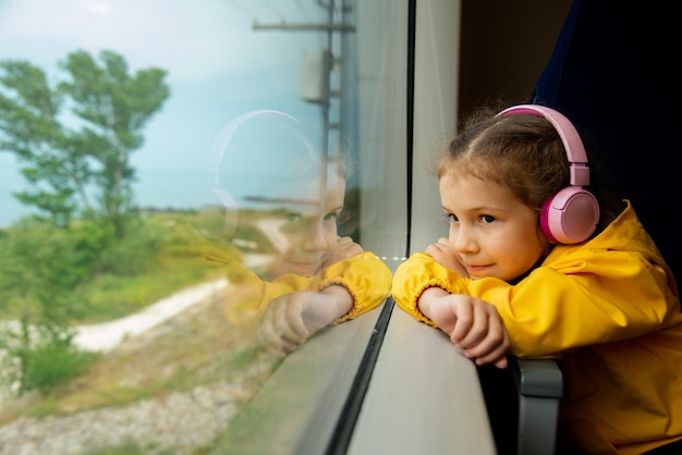 Dziewczyna w słuchawkach w pociągu wygląda przez okno. Podróż.