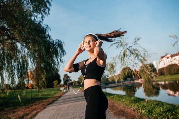 Dziewczyna w słuchawkach zajmuje się fitnessem na świeżym powietrzu w metropolii. bieganie i sport latem