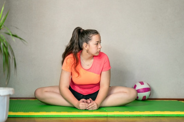 Dziewczyna w sportowym mundurze siedzi na macie i rozciąga się Koncepcja zdrowego stylu życia