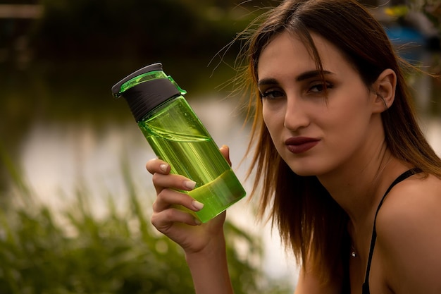 dziewczyna w sportowym stroju trzyma w dłoni butelkę, dziewczyna pije wodę z butelki
