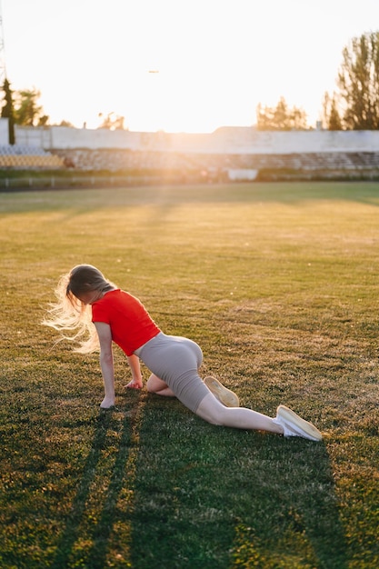 Dziewczyna w stroju sportowym rozciągająca się o zachodzie słońca Letni wieczór Dziewczyna na zielonej trawie ćwicząca przed słońcem