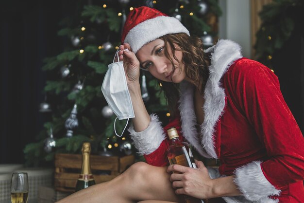 Dziewczyna w stroju Świętego Mikołaja zdjęła ochronną maskę medyczną na tle choinki w domu. koncepcja kwarantanny i samoizolacji na nowy rok i święta Bożego Narodzenia.