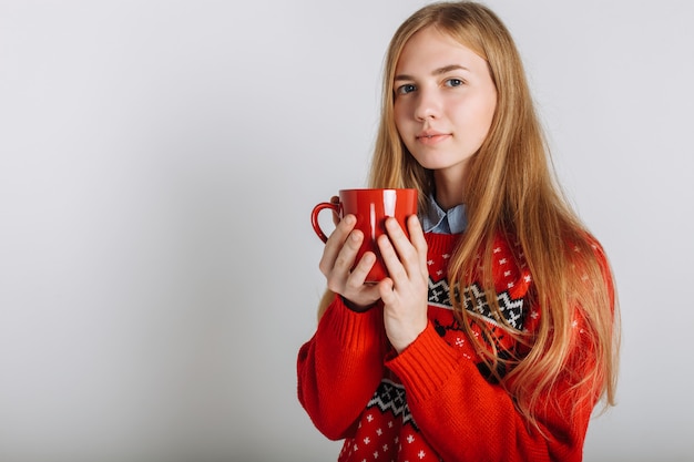 Dziewczyna w swetrze świątecznym lub noworocznym w studiu, trzymając filiżankę aromatycznej kawy. Pojedyncze miejsce na tekst Świąteczny nastrój.