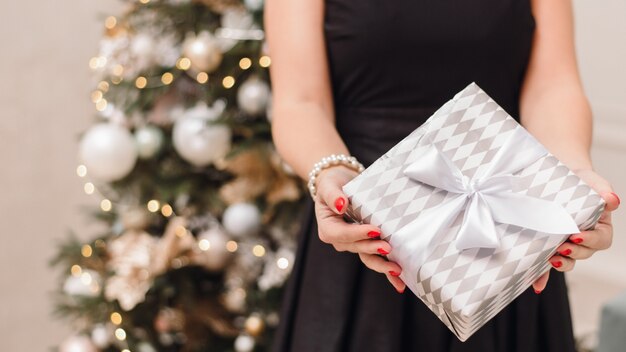 Zdjęcie dziewczyna w świątecznej czarnej sukni choinki z bokeh trzyma prezent
